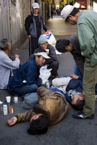 In a market street of Kamagasaki, homeless day laborers alert over one of them who is unconsious. The guy eventualy recovered but it was said that three other homeless people died that night because of the cold weather.